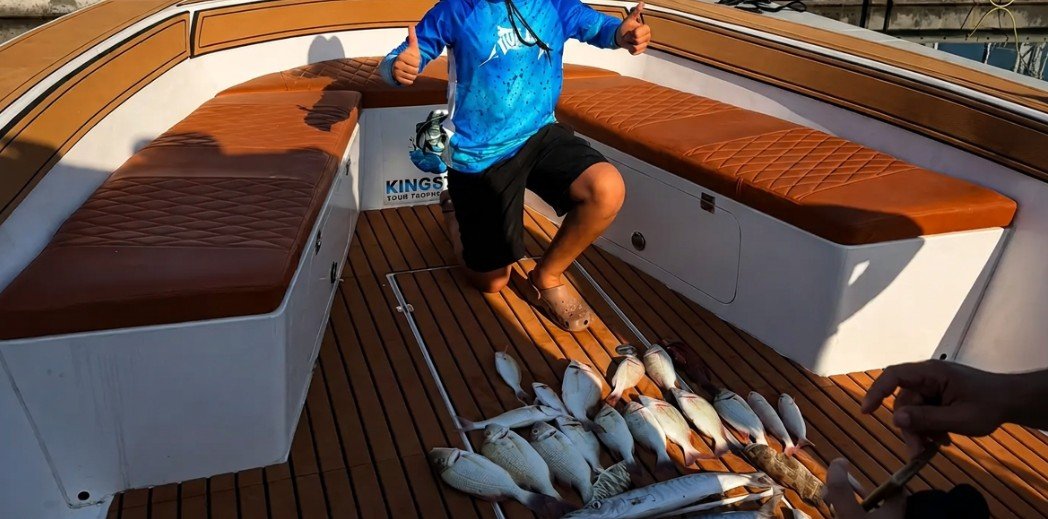 Young angler giving two thumbs up beside a big catch on the teak deck